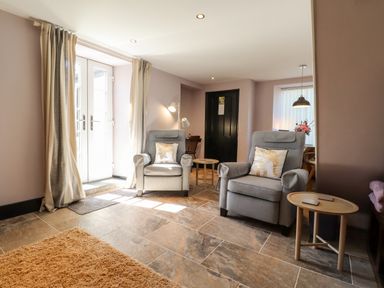 A sitting room with two armchairs each with an elephant pillow a small wooden table and a door with curtains at Morawel Fach in Newport Pembrokeshire