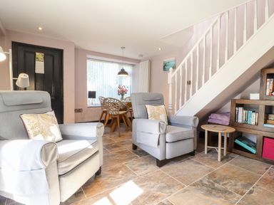A living room with two grey armchairs a dining table with chairs a staircase and a bookshelf at Morawel Fach in Newport Pembrokeshire