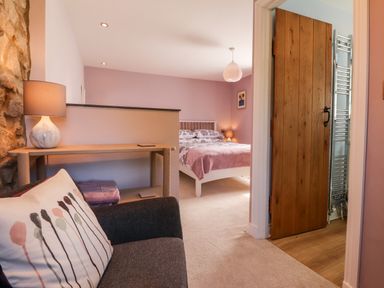 A bedroom with a bed side table lamp wooden door and a sofa with a cushion at Morawel Fach in Newport Pembrokeshire