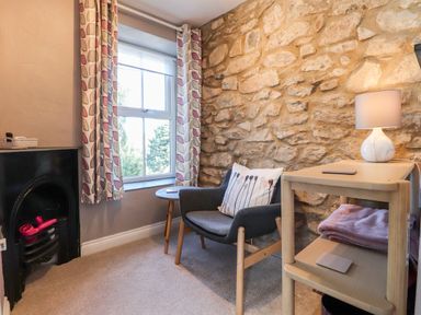 A small sitting area with a chair pillow lamp stone wall and window at Morawel Fach Newport Pembrokeshire