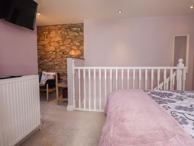 A bedroom with a bed with a pink throw and floral bedding a white railing a stone wall a chair and a small table at Morawel Fach in Newport Pembrokeshire