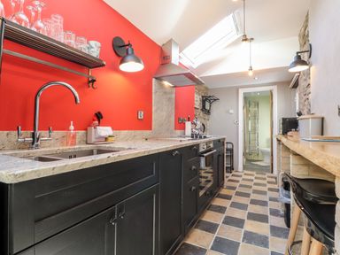 A kitchen with black cabinets a red wall a double sink an oven and a bar counter with stools at Morawel Fach in Newport Pembrokeshire