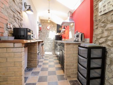 A narrow kitchen with brick walls black cabinets and checkered floor tiles at Morawel Fach in Newport Pembrokeshire