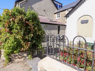 The exterior of a house with a wrought iron fence a gate climbing plants and a patio with chairs at Morawel Fach in Newport Pembrokeshire
