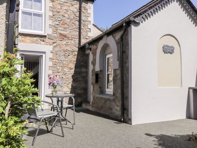 A stone and white exterior wall with a small table and chairs outside with flowers on the table at Morawel Fach in Newport Pembrokeshire