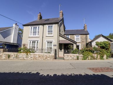A two-story house with stone and stucco exterior walls a small garden with flowers and a driveway with a vehicle at Morawel Fach in Newport Pembrokeshire
