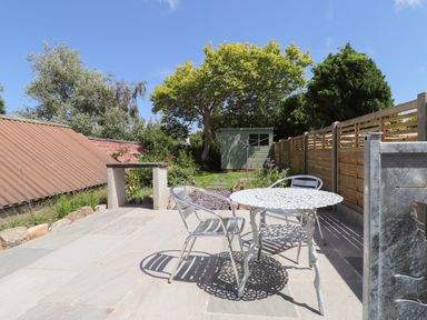 A patio with a round metal table and two metal chairs next to a garden with trees and a shed at Morawel Fach in Newport Pembrokeshire