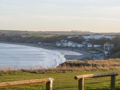 A coastal view with grassy area and wooden fence overlooking a bay with a beach and buildings at Silversands in Filey