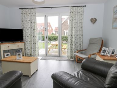 A living room with leather chairs a wooden coffee table a television and glass doors leading outside at Silversands in Filey