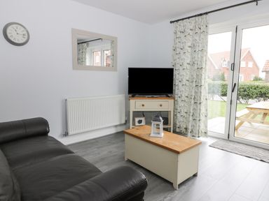A living room with a black sofa a coffee table a television on a stand and glass doors at Silversands in Filey