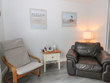 A corner with a wooden armchair with cushions a black leather armchair a small wooden side table with photo frames and a lamp Silversands Filey