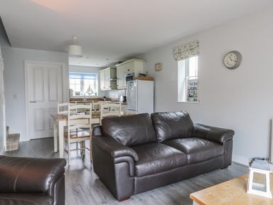 An open living room with dark leather sofas and a kitchen dining area with white chairs and cabinets at Silversands in Filey