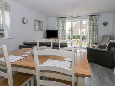A dining area with a wooden table and white chairs next to a living room with sofas a TV and glass doors at Silversands in Filey
