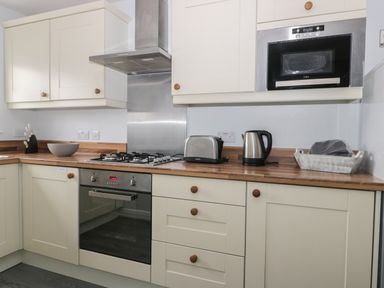 A kitchen with wooden countertops white cabinets a stove toaster kettle microwave and a knife block at Silversands in Filey