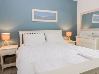A bedroom with a bed white bedding bedside tables table lamps a dresser a wall mirror and a framed picture at Silversands in Filey