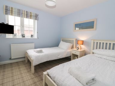 A bedroom with two single beds a nightstand with a lamp and clock and a window with striped blinds at Silversands in Filey
