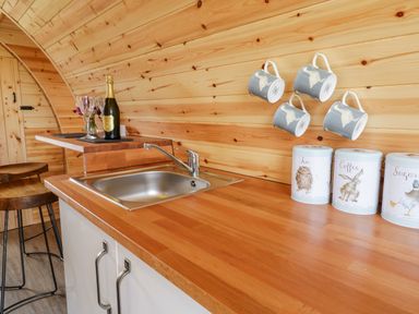 A wooden kitchen counter with a sink mugs hanging on the wall and storage tins at Embden Pod at Banwy Glamping in Llanfair Caereinion