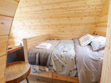A small bedroom with a wooden bed, printed bedding, folded towels, a wooden chair, and wooden walls at Embden Pod at Banwy Glamping in Llanfair Caereinion