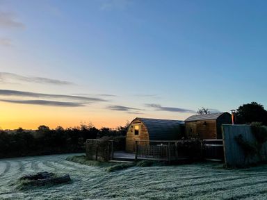 A wooden pod building with a wooden deck and frosted grass at sunrise at Embden Pod at Banwy Glamping in Llanfair Caereinion