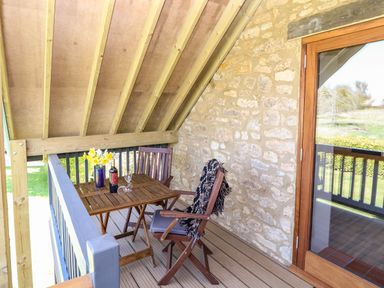 A covered balcony with wooden table and chairs stone wall and glass door at Cherrywood Barn in South Petherton