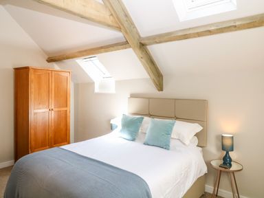 A bedroom with a bed with blue pillows a wooden wardrobe and a bedside table with a lamp at Cherrywood Barn in South Petherton