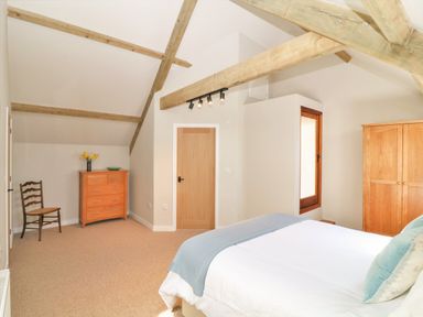 A bedroom with exposed wooden beams a bed a dresser a chair and a wardrobe at Cherrywood Barn in South Petherton