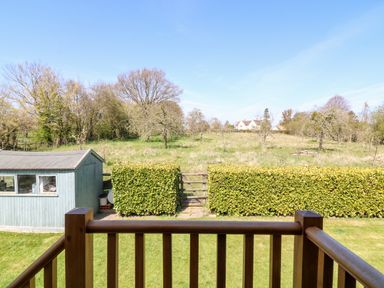 A backyard with a wooden railing shed trimmed hedges and a grassy field with trees and houses beyond at Cherrywood Barn in South Petherton