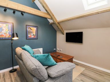 A living room with a gray sofa with blue cushions a wooden coffee table a floor lamp wall art and a wall-mounted TV at Cherrywood Barn in South Petherton