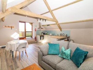 An open kitchen and living area with wooden beams a round dining table and a gray sofa with teal cushions at Cherrywood Barn South Petherton
