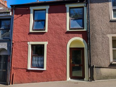 The exterior of a two story house with a red facade two windows and a door at Ty Coch y Castell in Pembroke