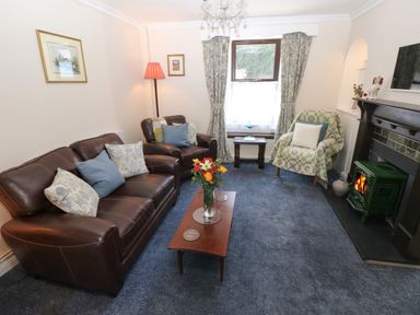 A living room with leather sofas a wooden coffee table with flowers and a stove at Ty Coch y Castell in Pembroke