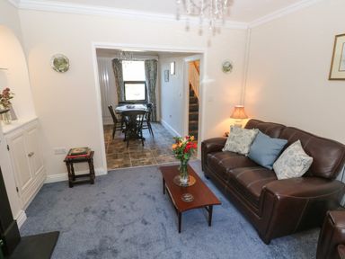 A living room with a brown leather sofa and a wooden coffee table next to a dining area with a table and chairs at Ty Coch y Castell in Pembroke