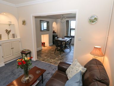 A living room with a brown leather sofa and a coffee table with flowers opening to a dining area with a wooden table and chairs at Ty Coch y Castell in Pembroke