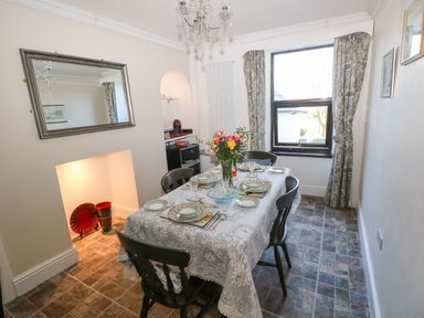 A dining room with a table set for six people and a window with curtains at Ty Coch y Castell in Pembroke