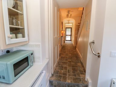 A hallway with tiled floor leading to a door with a microwave and cabinet on the left at Ty Coch y Castell in Pembroke