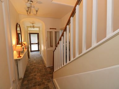 A hallway with stairs on the right and a door at the end with lamps on a shelf on the left at Ty Coch y Castell in Pembroke