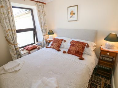 A bedroom with a double bed two bedside tables with lamps a window with curtains and a framed picture on the wall at Ty Coch y Castell in Pembroke