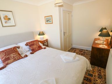A bedroom with a bed and red pillows bedside tables lamps a door and a dresser at Ty Coch y Castell in Pembroke
