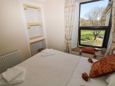 A bedroom with a bed with pillows and towels near a window with curtains and built in shelving at Ty Coch y Castell in Pembroke