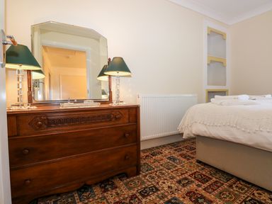 A bedroom with a wooden dresser with mirror and lamps a bed with white bedding and towel and patterned carpet at Ty Coch y Castell in Pembroke