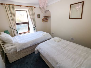 A bedroom with two single beds near a window with curtains and a mirror on the wall at Ty Coch y Castell in Pembroke