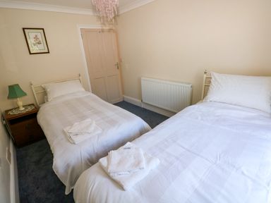 A bedroom with two single beds white bedding a nightstand with a green lamp and a framed picture on the wall at Ty Coch y Castell in Pembroke
