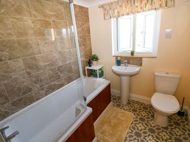A bathroom with a bathtub shower combination sink toilet and patterned floor tiles at Ty Coch y Castell in Pembroke