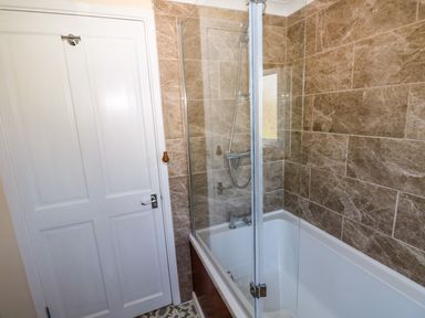 A bathroom with a bathtub shower combination and a white door at Ty Coch y Castell in Pembroke
