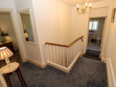 A hallway with carpeted floor a wooden railing a lamp on a side table and doorways to a bedroom and bathroom at Ty Coch y Castell in Pembroke