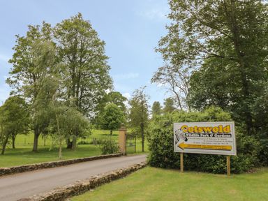 A road with stone walls on either side leading to gates and a sign for Cotswold Wildlife Park amp Gardens in Church Westcote near Bourton-On-The-Water