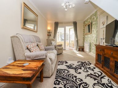 A living room with upholstered armchairs wooden table patterned rug and a television at Molly's Bit in Church Westcote near Bourton-On-The-Water