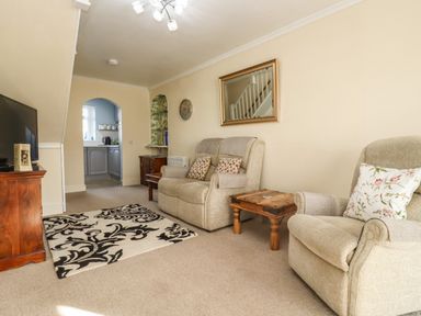 A living room with armchairs a wooden side table a TV on a wooden cabinet and a patterned rug at Molly's Bit in Church Westcote near Bourton-On-The-Water