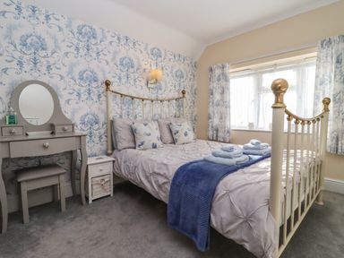 A bedroom with a bed with pillows and towels a dressing table and a window with curtains at Molly's Bit in Church Westcote near Bourton-On-The-Water