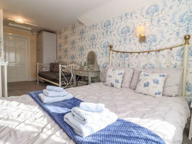 A bedroom with a double bed with towels on a blue runner and a daybed against a floral wallpaper at Molly's Bit in Church Westcote near Bourton-On-The-Water